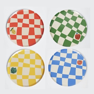 May include: Four round checkered plates with different coloured backgrounds and a small fruit or vegetable illustration on each. The plates are red, green, yellow, and blue.