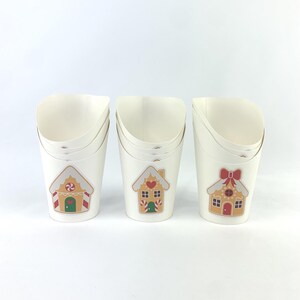 Puede incluir: Tres vasos de papel blancos con dise&ntilde;os de casas de jengibre. Cada vaso tiene un dise&ntilde;o diferente con una casa de jengibre con detalles de caramelo. Los vasos est&aacute;n apilados uno encima del otro.