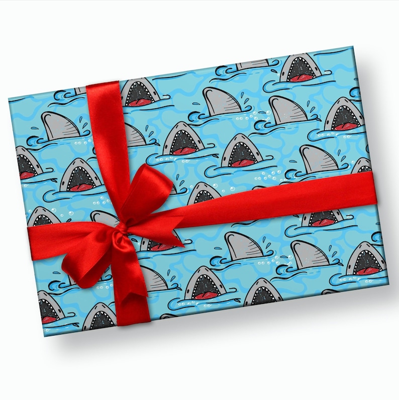 May include: A blue gift wrap with a red ribbon and a pattern of cartoon sharks with open mouths. The sharks are swimming in blue water with white bubbles.