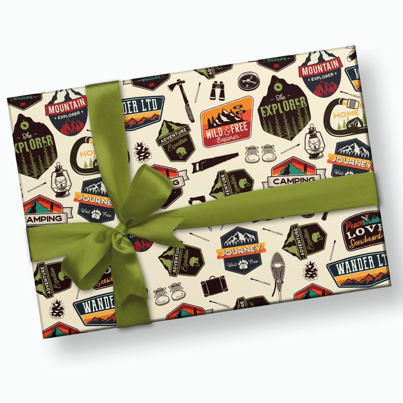May include: A cream-colored gift wrap with a repeating pattern of colorful vintage-style camping and adventure themed logos. The logos feature text such as "The Explorer", "Mountain Explorer", "Wild & Free Explorer", "Journey", "Camping", "Adventure Expedition", and "Wander LTD". The gift wrap is tied with a green ribbon.
