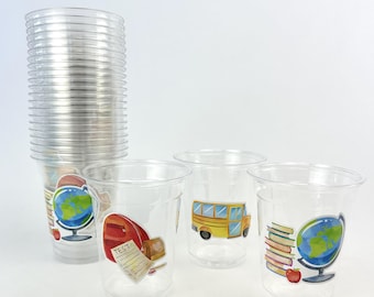 May include: Clear plastic cups decorated with school-themed stickers. Designs feature a globe, books, a red apple, a school bus, and a backpack with a test paper. A stack of cups is on the left.