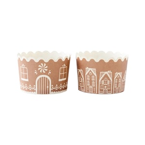 May include: Two brown paper cupcake liners with white gingerbread house designs. One liner features a single house with a candy cane and a door. The other liner features a row of houses.