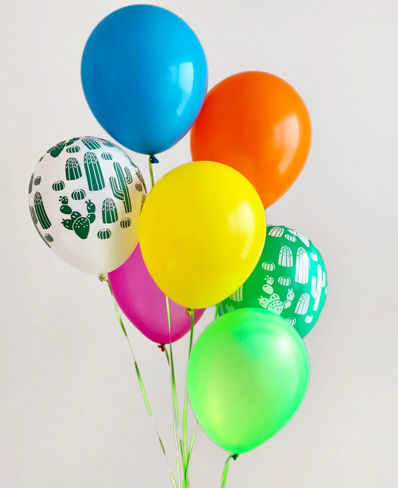 Puede incluir: Un grupo de seis globos, que incluyen un globo azul, un globo naranja, un globo amarillo, un globo rosa, un globo verde y un globo blanco con un patr&oacute;n de cactus verde.