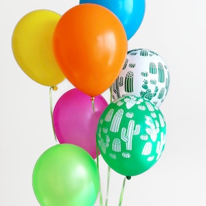 Puede incluir: Un mont&oacute;n de globos de colores, incluyendo verde, amarillo, naranja, rosa y azul, con un globo que presenta un patr&oacute;n de cactus blanco sobre un fondo verde.