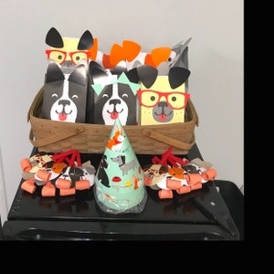 May include: A set of party favor bags featuring cartoon dogs wearing glasses and hats. The bags are in a wicker basket with a party hat on top. There are also several party favors with dog illustrations.