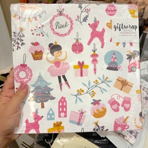 May include: A white gift wrap with a pink ballerina, reindeer, and Christmas ornaments. The wrapping paper has the text "Noel" and "giftwrap boutique wrapping paper 3 sheets - 30" x 20".