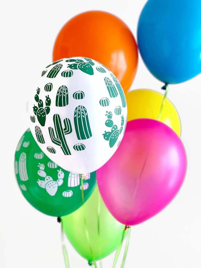 Puede incluir: Un grupo de globos coloridos con un patr&oacute;n de cactus y fresas. Los globos son verdes, blancos, naranjas, rosas, amarillos y azules.