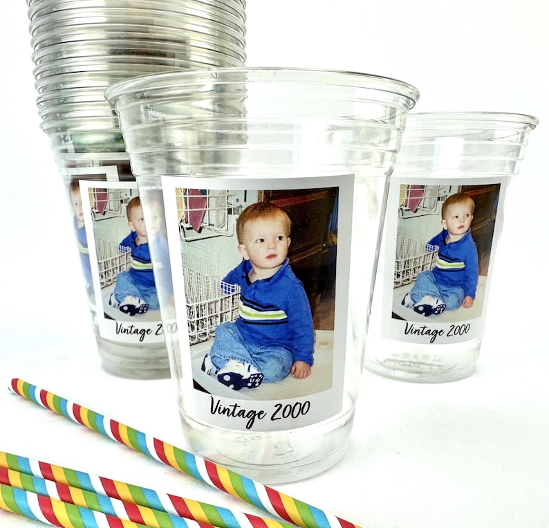 Puede incluir: Vasos de pl&aacute;stico transparente con una foto de un ni&ntilde;o peque&ntilde;o y el texto "Vintage 2000". El ni&ntilde;o lleva una camisa azul y vaqueros. Hay pajitas de colores a rayas en primer plano.