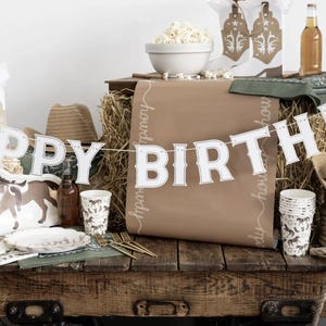 May include: A rustic birthday party setup with a western theme. Includes a banner that says "HAPPY BIRTHDAY", cowboy hats, horse-shaped plates, and paper cups. A bowl of popcorn and a bottle of beer are also visible.