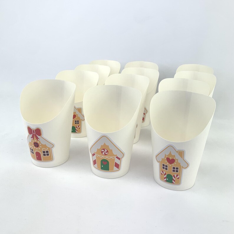 Puede incluir: Diez vasos de papel blancos con un dise&ntilde;o de casa de jengibre. Los vasos son perfectos para contener peque&ntilde;os bocadillos o golosinas.