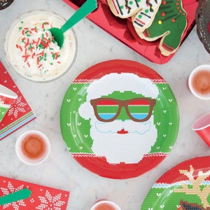 Pu&ograve; includere: Piatti di carta rossi e verdi con un design natalizio a tema maglione. Un piatto presenta un Babbo Natale con occhiali da sole, un altro piatto presenta una renna.