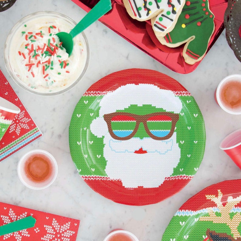 Pu&ograve; includere: Piatti di carta rossi e verdi con un design natalizio a tema maglione. Un piatto presenta un Babbo Natale con occhiali da sole, un altro piatto presenta una renna.