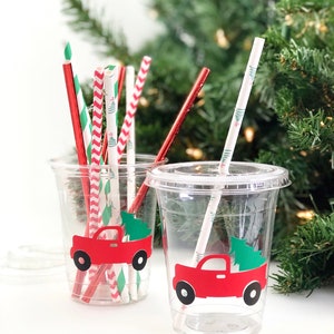 K&ouml;nnte beinhalten: Zwei durchsichtige Plastikbecher mit roten Lastwagen- und Weihnachtsbaummotiven. Die Becher sind mit rot-wei&szlig; gestreiften Papierstrohhalmen, gr&uuml;n-wei&szlig; gestreiften Papierstrohhalmen und einfarbigen roten Papierstrohhalmen gef&uuml;llt.