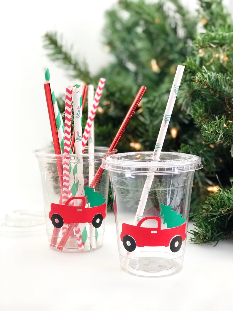 K&ouml;nnte beinhalten: Zwei durchsichtige Plastikbecher mit roten Lastwagen- und Weihnachtsbaummotiven. Die Becher sind mit rot-wei&szlig; gestreiften Papierstrohhalmen, gr&uuml;n-wei&szlig; gestreiften Papierstrohhalmen und einfarbigen roten Papierstrohhalmen gef&uuml;llt.