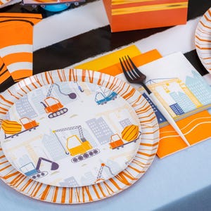 May include: A set of construction-themed party supplies. Includes paper plates with orange and white striped rims and construction vehicle graphics. Napkins, forks, and orange accents complete the table setting. The plates feature illustrations of construction vehicles and cityscapes.