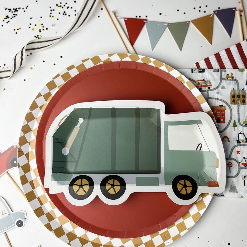 May include: Red and white checkered paper plate with a green and white garbage truck design. The truck has a red, white, and blue flag on the back.