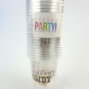 Puede incluir: Una pila de vasos de fiesta de pl&aacute;stico transparente envueltos en pl&aacute;stico. Las tazas tienen un dise&ntilde;o "Howdy" en marr&oacute;n y dorado. Una etiqueta en el embalaje dice "STESHA PARTY! PARTY SUPPLIES + DECORATIONS."