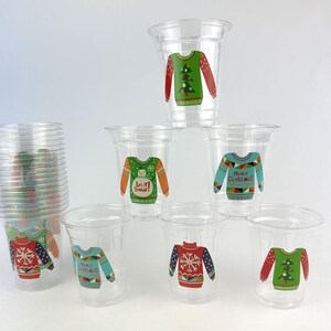 May include: Clear plastic cups with festive Christmas sweater designs. The sweaters feature various patterns, including snowflakes, Christmas trees, and the text "Merry Christmas" and "Let it Snow!" These cups are ideal for holiday gatherings and parties.