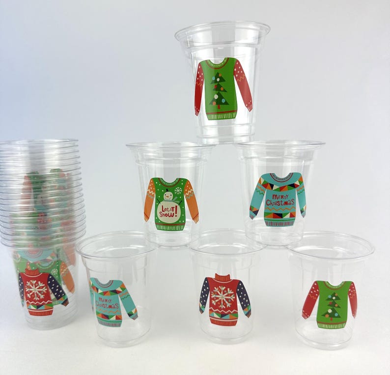 May include: Clear plastic cups with festive Christmas sweater designs. The sweaters feature various patterns, including snowflakes, Christmas trees, and the text "Merry Christmas" and "Let it Snow!" These cups are ideal for holiday gatherings and parties.