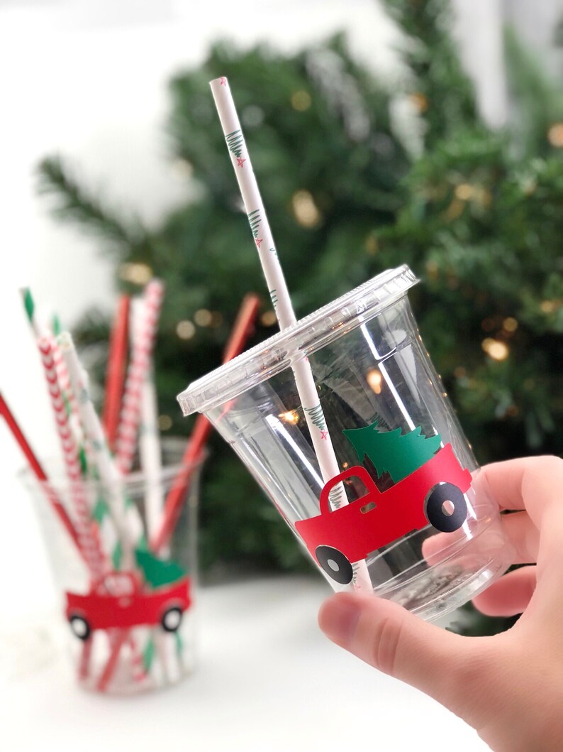 K&ouml;nnte beinhalten: Zwei durchsichtige Plastikbecher mit roten Lastwagen-Weihnachtsbaum-Designs. Die Becher haben rot-wei&szlig; gestreifte Strohhalme.