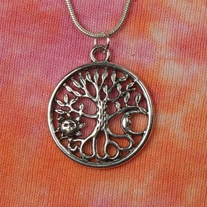 May include: Silver necklace with a circular pendant featuring a tree of life design. The tree has a sun and moon on either side of the trunk.