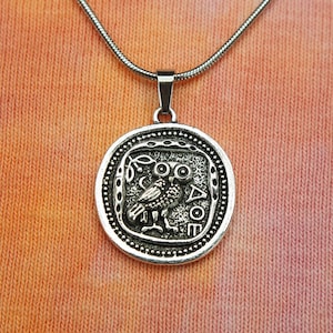May include: Silver necklace with a round pendant featuring an owl and the Greek word "ATHENE".
