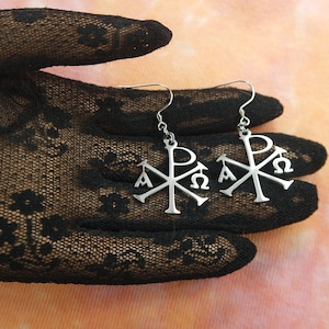 May include: A pair of silver earrings with a Christian symbol, the Chi Rho, featuring the Greek letters Alpha and Omega.