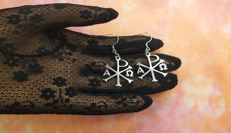 May include: A pair of silver earrings with a Christian symbol, the Chi Rho, featuring the Greek letters Alpha and Omega.