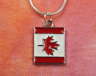 Könnte beinhalten: Eine silberne Kettenkette mit einem roten und weißen Emaille-Anhänger mit der kanadischen Flagge. Der Anhänger ist quadratisch mit einem roten Ahornblatt auf weißem Hintergrund.