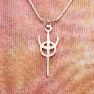 Può includere: Una collana d'argento con un ciondolo a forma di spada stilizzata con un cerchio al centro. Il ciondolo è su una catena d'argento.