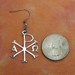 May include: Silver earring with a Chi Rho symbol, a Christian symbol that represents the first two letters of Christ's name in Greek, with the letters Alpha and Omega on either side. The earring is about the size of a quarter.