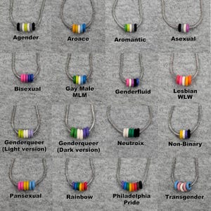 May include: A collection of silver necklaces, each featuring a pendant of colorful beads. The necklaces are labeled with terms such as "Agender," "Bisexual," and "Rainbow." The pendants have various color combinations, including pink, blue, and orange.