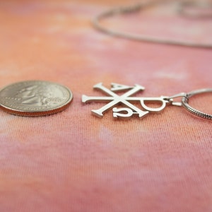 May include: A silver chain necklace with a silver pendant featuring the Chi Rho symbol, a Christian symbol representing Christ.
