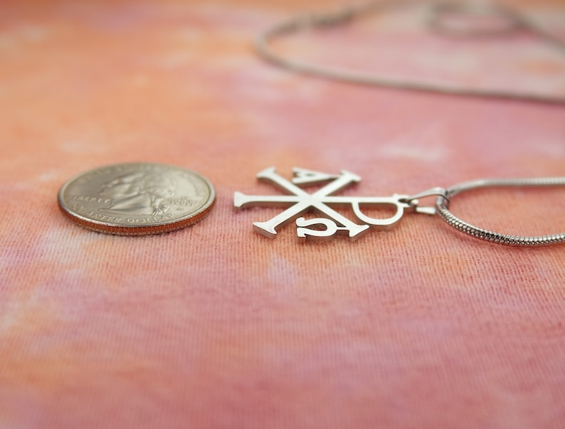 May include: A silver chain necklace with a silver pendant featuring the Chi Rho symbol, a Christian symbol representing Christ.