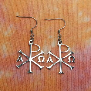 May include: A pair of silver earrings with a stylized Christian symbol, the Chi Rho, with the Greek letters Alpha and Omega.