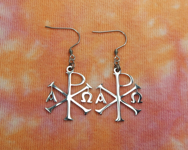 May include: A pair of silver earrings with a stylized Christian symbol, the Chi Rho, with the Greek letters Alpha and Omega.
