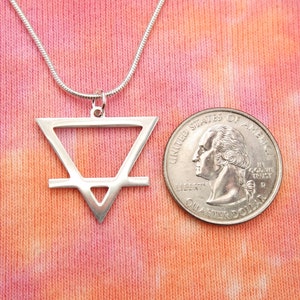 May include: A silver necklace with a geometric pendant in the shape of a triangle with a horizontal line through the middle. The pendant is about the size of a US quarter.