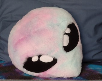 May include: A plush alien-shaped cushion with a pink, blue and white tie-dye pattern. The cushion has large black eyes with white highlights.