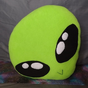 May include: A bright green plush alien pillow with black eyes and a white smile. The pillow is soft and cuddly and would make a great gift for any alien fan.