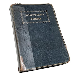May include: A vintage hardcover book titled Whittier's Poems with a dark blue, textured cover. The front cover features gold lettering enclosed in a decorative border. The spine area shows signs of wear with visible tape and exposed material.