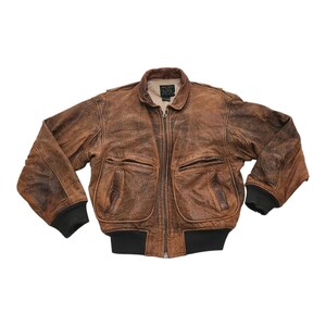 May include: A brown leather bomber jacket with a distressed finish. The jacket has a zip-up front, two front pockets, and black ribbed cuffs and hem. The collar is a classic fold-down style.