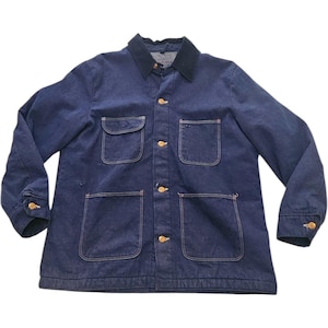 Puede incluir: Una chaqueta de trabajo de mezclilla azul oscuro con un cuello de pana azul marino en contraste, mangas largas con puños abotonados y cuatro bolsillos delanteros de parche. La chaqueta se cierra con cinco botones de metal dorado.
