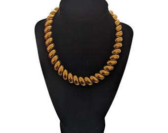 May include: A gold-toned necklace with a chunky, twisted chain design. The necklace is displayed on a black velvet mannequin bust.