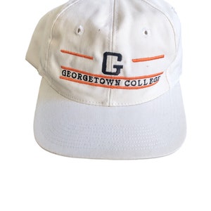 May include: A white baseball cap with an orange and navy blue embroidered logo that reads "GEORGETOWN COLLEGE" and a navy blue "G" in the center.