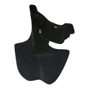 May include: A single gold-toned earring with a pink gemstone is displayed on a black jewelry bust. The earring has a small, rectangular shape with a pink stone. The bust is a dark, velvety material.
