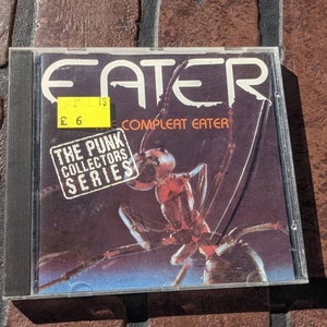 May include: A black CD case with a red ant on the cover. The title "EATER" is printed in white letters. The text "COMPLEAT EATER" is printed in white letters below the title. The text "THE PUNK COLLECTORS SERIES" is printed in a white rectangle in the lower left corner.