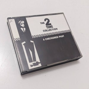 Può includere: Una custodia per CD in bianco e nero con un'illustrazione in bianco e nero di una persona con cappello e abito. Il testo sulla custodia recita "The 2 Tone Collection A Checkered Past".