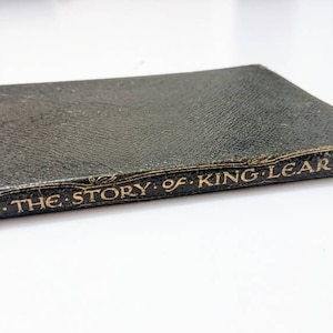 Puede incluir: Un libro antiguo encuadernado en cuero negro con letras doradas en el lomo que dice "THE STORY OF KING LEAR."