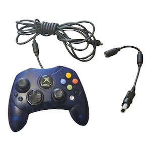 Pode incluir: Um controle Xbox azul escuro com um cabo preto e um adaptador separado. O controle possui um direcional preto, dois manípulos analógicos e botões de ação coloridos. O logotipo do Xbox está no centro.