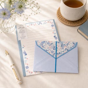 May include: A stationery set featuring a light blue envelope with a floral patterned flap secured by a blue elastic band, and a matching lined writing sheet with floral borders. The sheet includes text reading Rilette Flower Patterns Made in Japan.